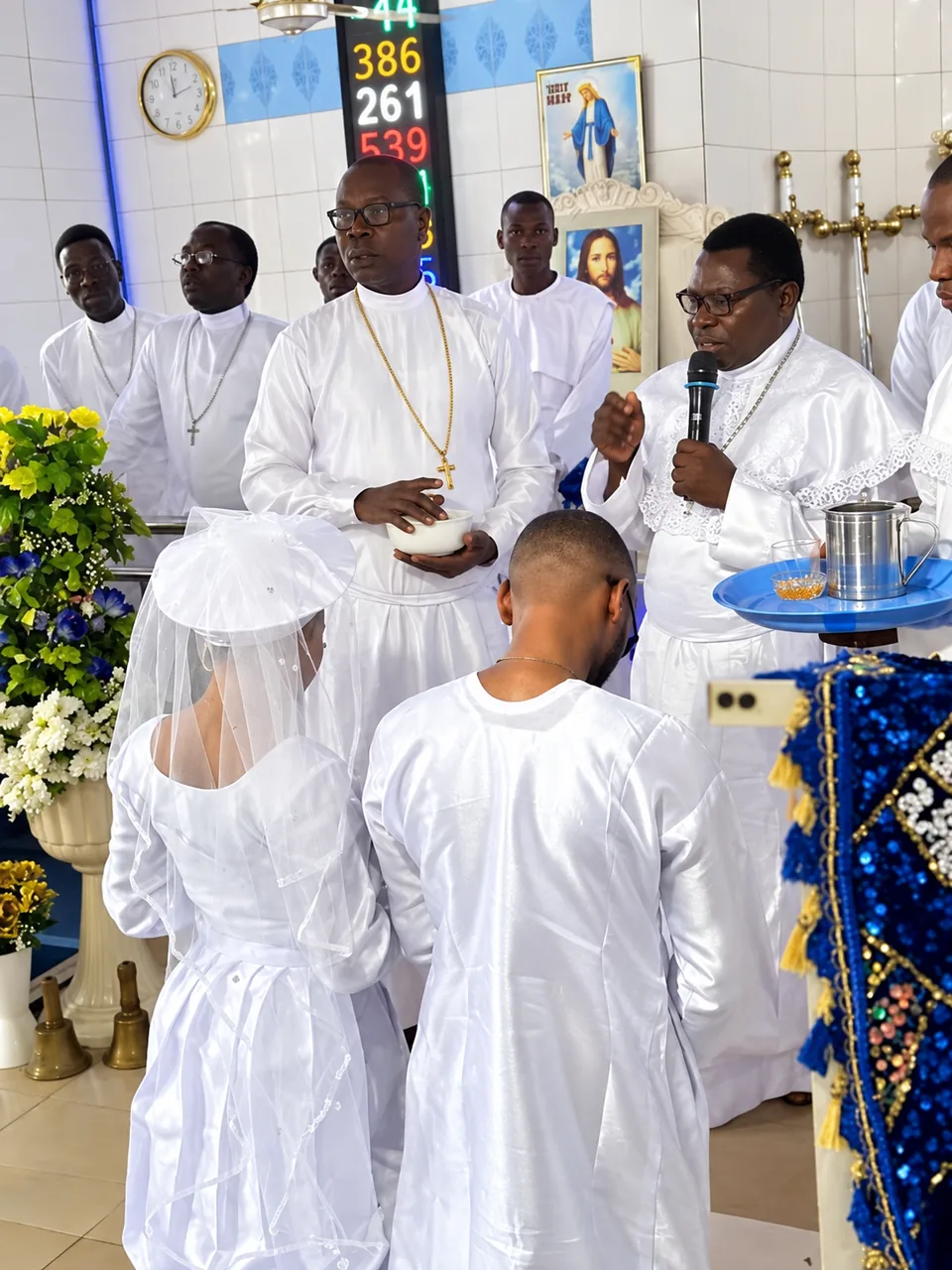 A couple stand with heads bowed before ministers in white at an altar dressed in blue and gold